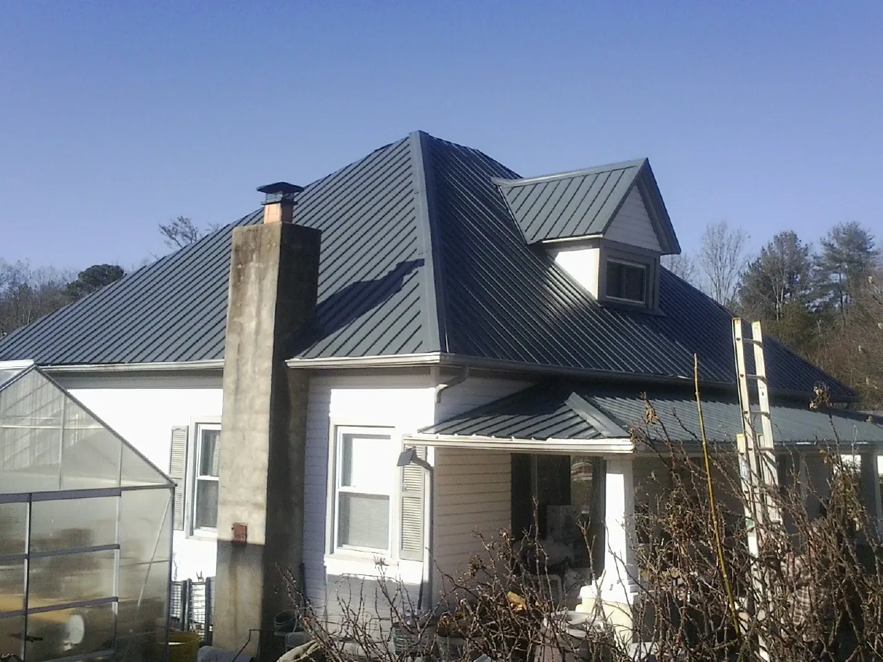 Dark blue standing seam metal roof on a white farmhouse with dormer — Slate & Tile Roof Repair by Roofing Brothers in Normalville