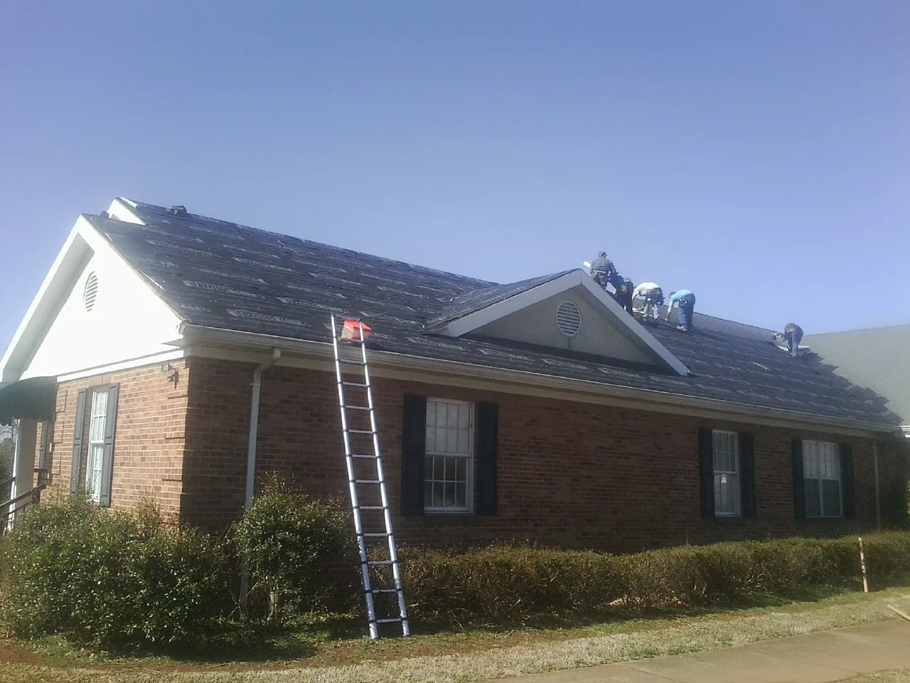 Crew tearing shingles off a brick ranch roof with a ladder set — Metal Roof Repair work by our crew in Normalville