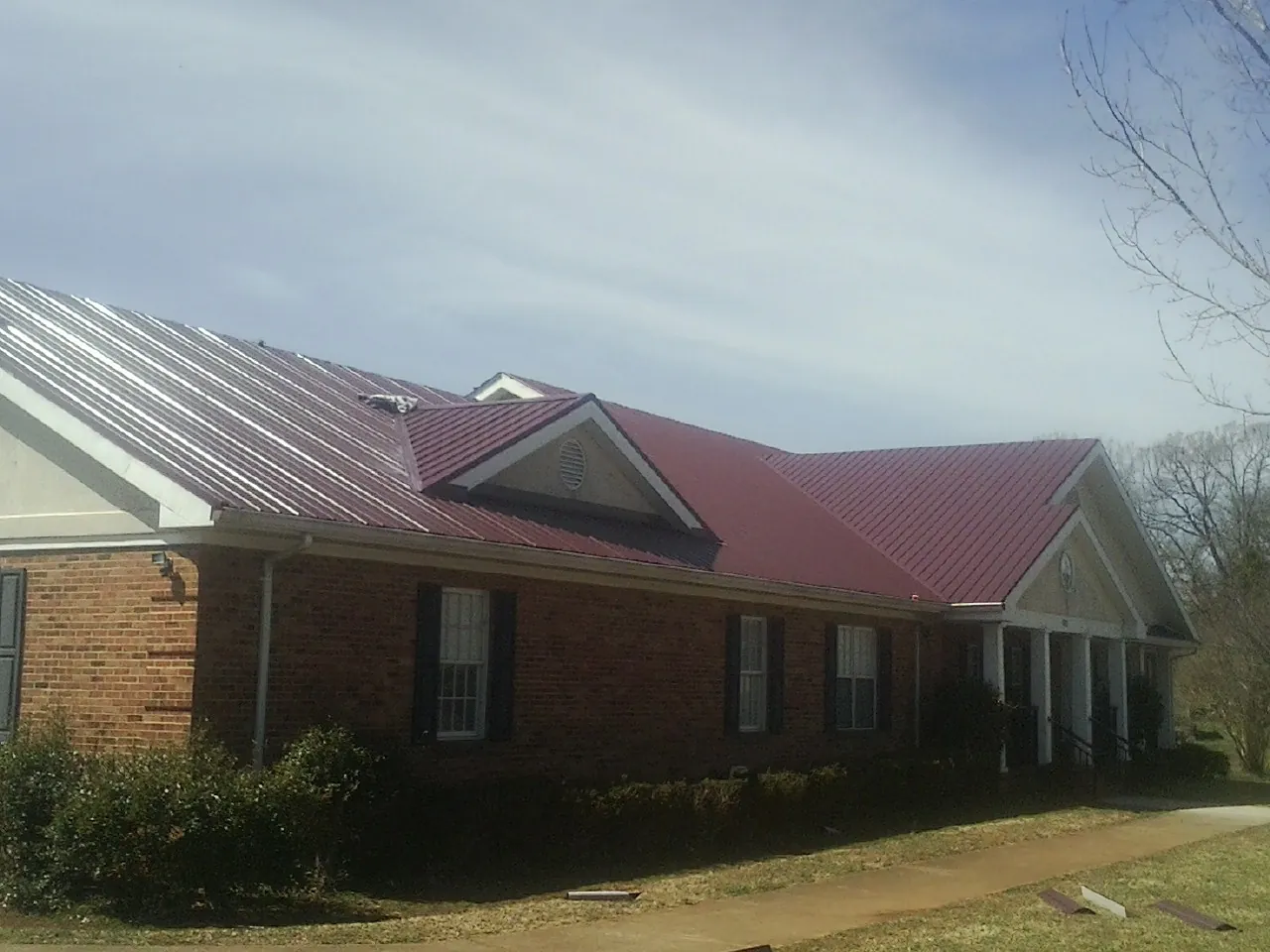 Red metal roof with gabled entries on a long brick building, from a Hail Damage Roof Repair job in Normalville