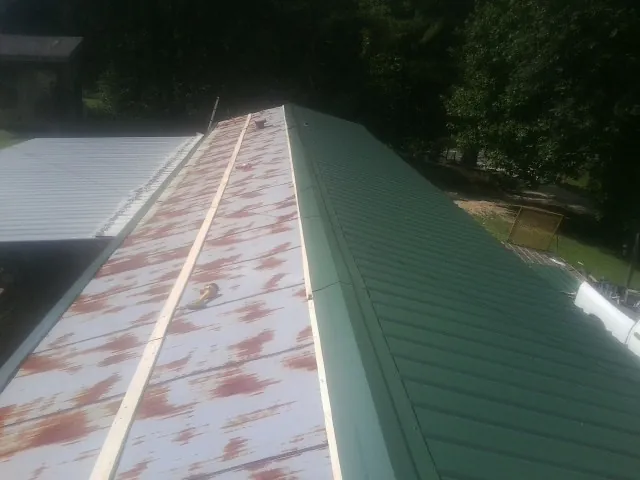 Old rusted panels beside newly installed green metal roofing — Wind Damage Roof Repair by Roofing Brothers in Normalville