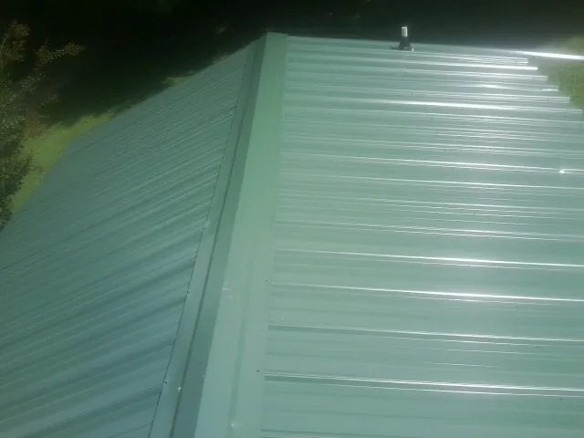 New green metal panels meeting at the ridge of a roof — Flat Roof Repair work by our crew in Normalville
