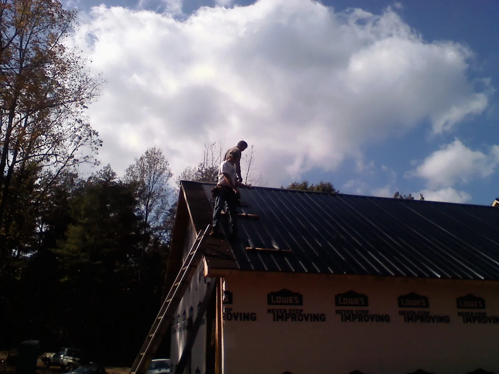Roofer fastening dark metal panels high against a cloudy sky, from a Roof Inspection job in Normalville