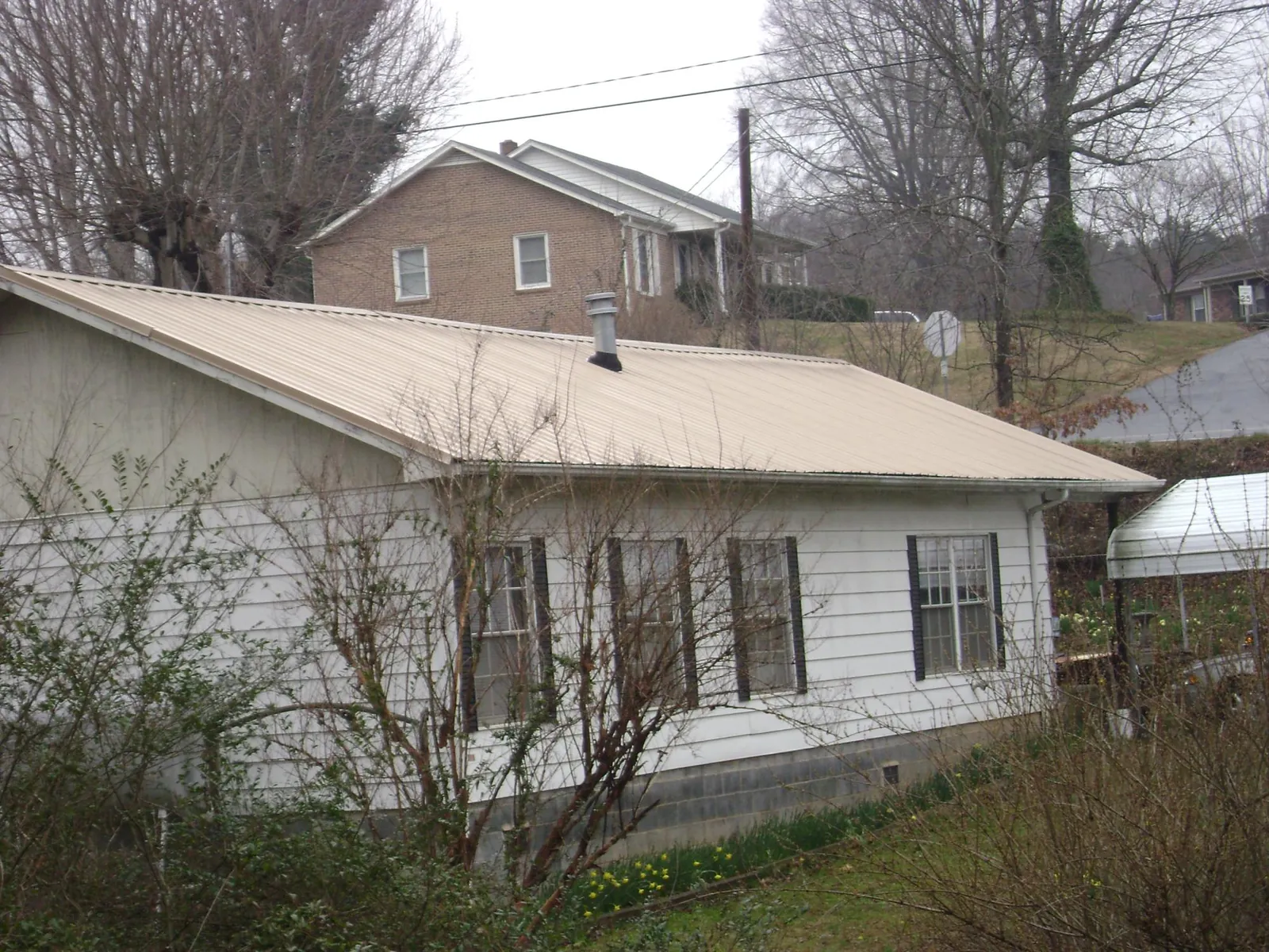 Tan metal roof on a white sided house set into a hillside — Commercial Roofing by Roofing Brothers in Normalville