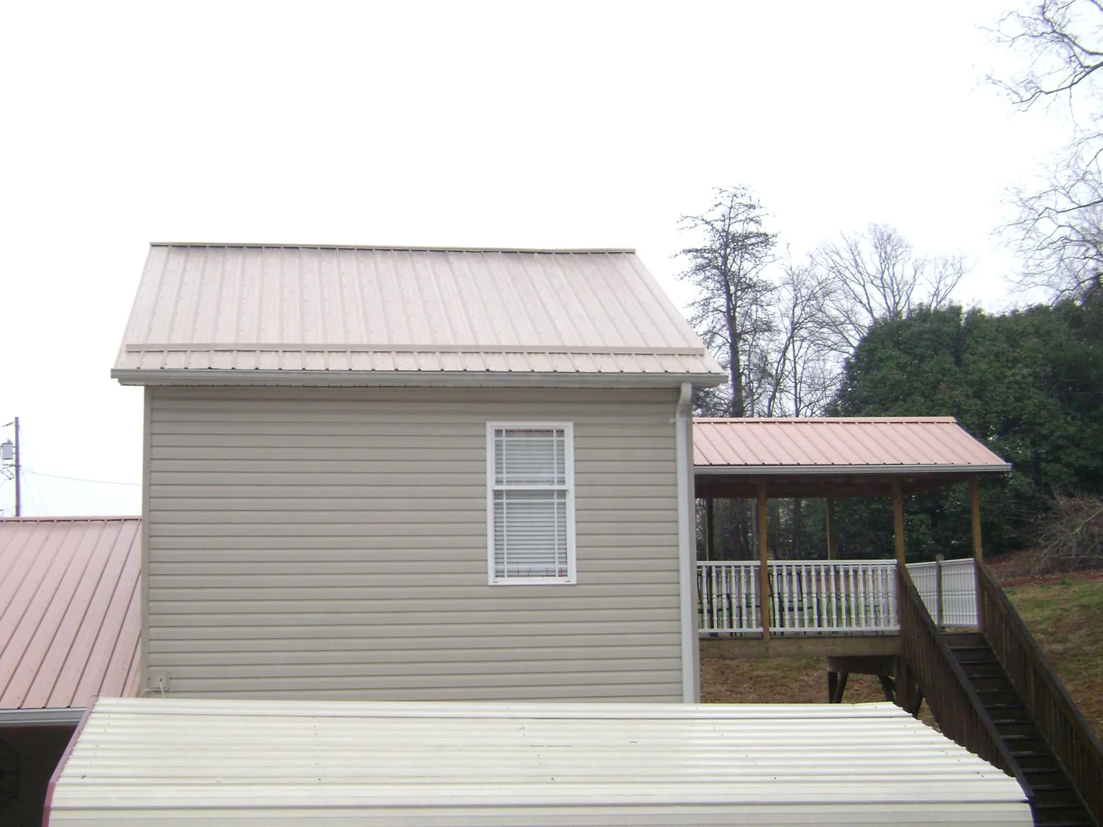 Tan metal roofs on a two story addition and attached porch, from a Roof Replacement job in Normalville
